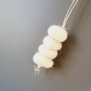 May include: A white felt Christmas tree ornament with a small silver animal charm hanging from the bottom.