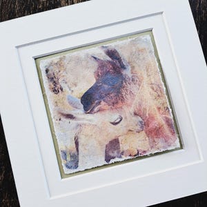 May include: A framed watercolor painting of two llamas, one with its head resting on the other's neck. The painting has a soft, vintage feel with muted colors of pink, blue, and brown.