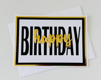 May include: A birthday greeting card with the word "BIRTHDAY" in bold black letters and the word "happy" in gold script. The card has a gold border and is on a white background with a white envelope.