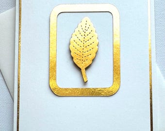 May include: A white card with a gold border and a gold leaf design inside a gold frame.