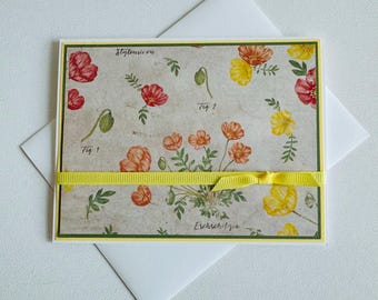 May include: A greeting card with a floral pattern featuring red and yellow flowers. The card has a yellow ribbon tied around it and the text "Eschscholzia" is printed on the bottom.