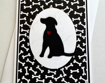 May include: A black and white greeting card with a silhouette of a dog sitting on a white cloud with a red heart. The background is a black and white pattern of dog bones.