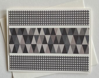 May include: A greeting card with a geometric design. The card features a white border with a gray dotted pattern at the top and bottom. The center has a pattern of gray triangles. The card is placed on a white envelope.