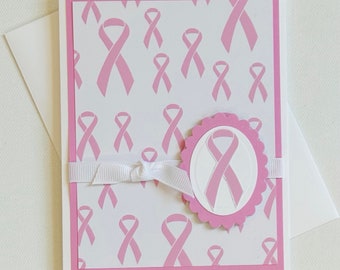 May include: Pink card with a pink ribbon pattern and a large pink ribbon with a white outline in the center. The card has a white ribbon tied around it.