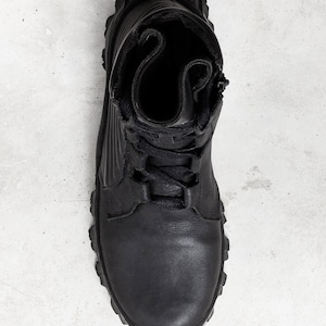 May include: Black leather boot with a rugged sole, laces, and a side zipper. The boot has a high-top design and a textured upper. The overall style is utilitarian and durable, suitable for outdoor activities or work.