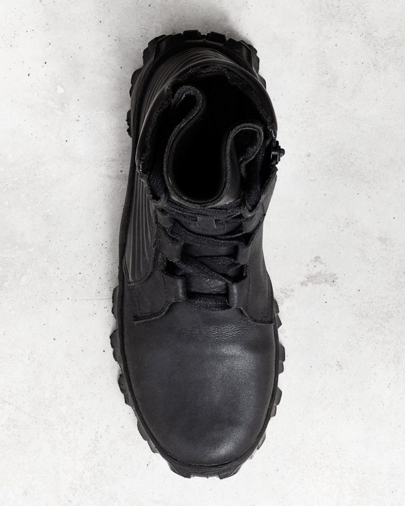 May include: Black leather boot with a rugged sole, laces, and a side zipper. The boot has a high-top design and a textured upper. The overall style is utilitarian and durable, suitable for outdoor activities or work.
