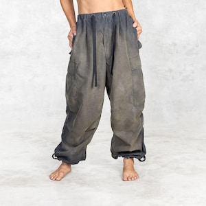 Puede incluir: Pantalones cargo grises con efecto degradado descolorido. Los pantalones tienen cintura con cordón, bolsillos laterales y cordones en los tobillos. La tela parece ser un material suave y ligero.