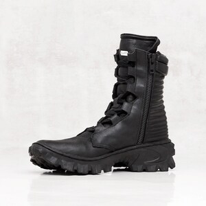 May include: Black leather combat boot with a side zipper, lace-up front, and a rugged, ridged sole. The boot features a high shaft and a padded collar. The boot is designed for durability and style.