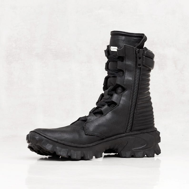 May include: Black leather combat boot with a side zipper, lace-up front, and a rugged, ridged sole. The boot features a high shaft and a padded collar. The boot is designed for durability and style.