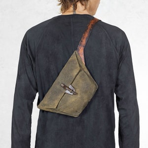 Puede incluir: Bolso bandolera verde oliva con correa de cuero y cierre de metal. El bolso se lleva en diagonal sobre el cuerpo. La correa es marr&oacute;n con un patr&oacute;n texturizado. El bolso tiene forma triangular.