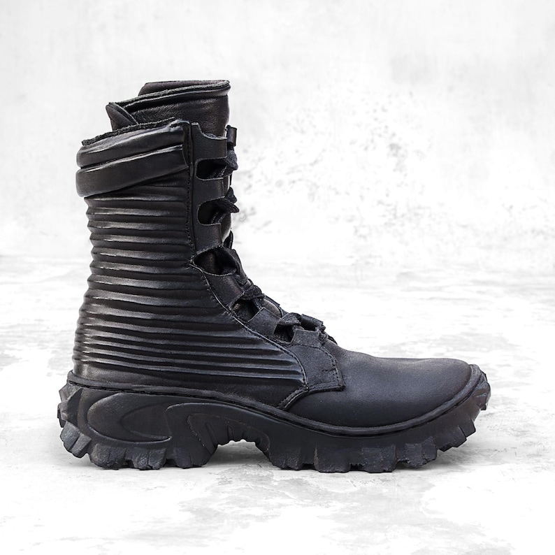 May include: Black combat boot with a ridged shaft and a thick, lugged sole. The boot features a lace-up closure and multiple straps. The upper is made of a matte material, and the boot has a high-top design.