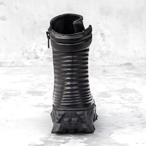 May include: Black leather boot with a ridged shaft and a rugged, textured sole. The boot features a side zipper and a padded collar. The design is modern and edgy, suitable for various fashion styles.