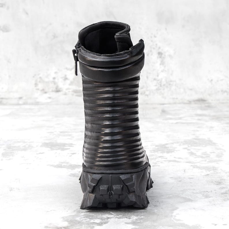 May include: Black leather boot with a ridged shaft and a rugged, textured sole. The boot features a side zipper and a padded collar. The design is modern and edgy, suitable for various fashion styles.