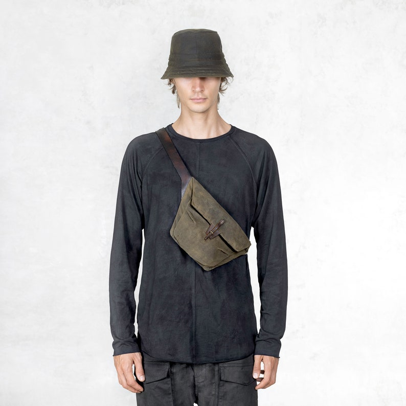 Puede incluir: Una persona con un sombrero de pescador verde oscuro, una camiseta negra de manga larga y una ri&ntilde;onera verde-marr&oacute;n con correa y hebilla de cuero. La ri&ntilde;onera se lleva cruzada sobre el pecho.