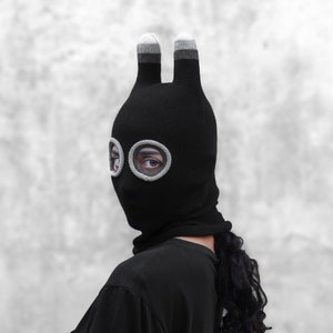 May include: Black knit balaclava with bunny ears and two circular eye holes. The balaclava is made of a soft, stretchy fabric and has a gray trim around the eye holes.
