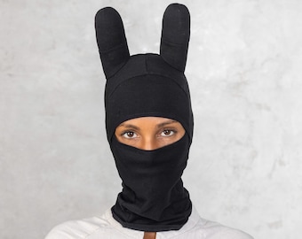 May include: A black balaclava with bunny ears. The balaclava covers the person's face, leaving only their eyes visible.