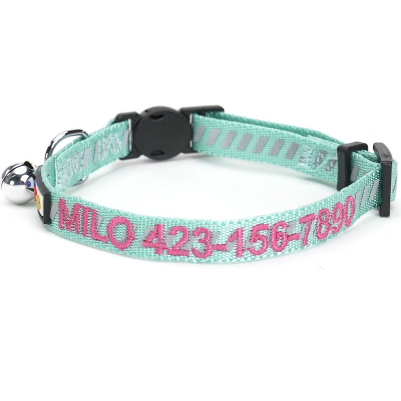 May include: A light blue cat collar with a safety breakaway buckle and a bell. The collar is personalised with the name "MILO" and the phone number "423-456-7890" in pink thread.