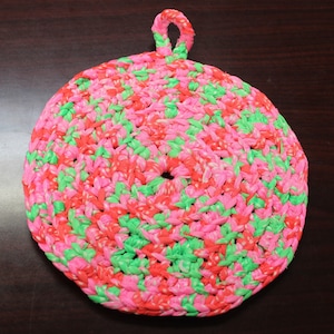 Puede incluir: Un posavasos de ganchillo rosa y verde con un asa de bucle. El posavasos está hecho de hilo y tiene una forma circular.