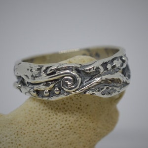 May include: A silver ring with a textured, organic design featuring a spiral and small beads.