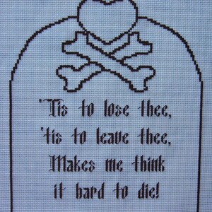 Op de afbeelding: Borduurwerk met kruissteek op blauwe stof met een zwart hart- en kruisbeenderenmotief. De tekst luidt: 'Tis to lose thee, 'tis to leave thee, Makes me think it hard to die!'