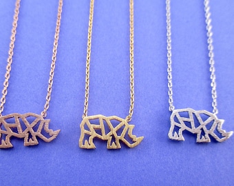 May include: Three necklaces with rhino pendants in rose gold, gold, and silver. Each pendant features a geometric design of a rhino on a delicate chain. The necklaces are displayed on a blue background.