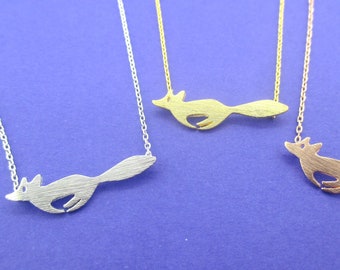 Peut inclure: Trois colliers avec des pendentifs renard. Les pendentifs sont en argent, or et or rose. Chaque pendentif renard est relié à une chaîne délicate. Le fond est de couleur bleu uni.