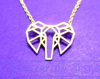 May include: A gold-colored necklace with a geometric elephant pendant. The pendant is made of interconnected lines forming the shape of an elephant's head. The necklace is on a purple background.