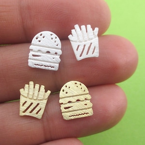 May include: Four small, detailed food-themed earrings. Two silver-colored earrings depict a hamburger and a container of french fries. The other two earrings are gold-colored, with a hamburger and a container of french fries.