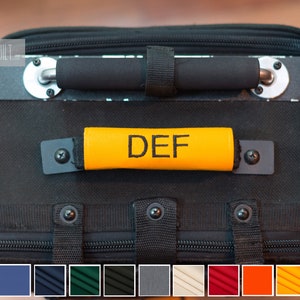 May include: Black travel bag with a yellow handle strap that says "DEF" in black lettering. The bag has a zipper and multiple straps. The bag is shown against a wood background. The image also includes a color swatch of 10 different colors.