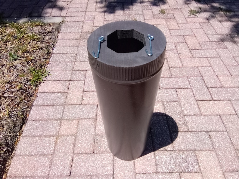 May include: A brown cylindrical container with a black foam top and two metal hooks. The container is sitting on a brick patio.