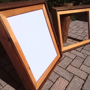 May include: Two wooden picture frames, one larger than the other, with a natural wood finish. The larger frame is brown with a light brown inner border. The smaller frame is brown with a light brown inner border. Both frames are empty.