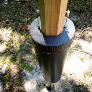 May include: Close-up of a black post protector with metal brackets securing it to a wooden post.