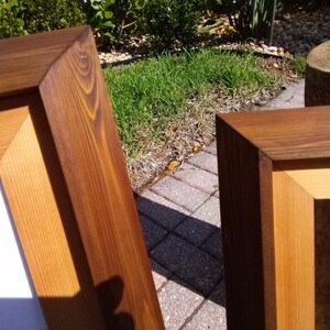 Może przedstawiać: Dwa drewniane ramki na zdjęcia z naturalnym wykończeniem drewna. Ramki wykonane są z litego drewna i mają prosty, klasyczny design.