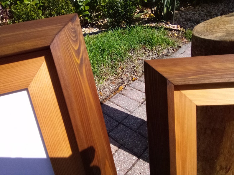 Może przedstawiać: Dwa drewniane ramki na zdjęcia z naturalnym wykończeniem drewna. Ramki wykonane są z litego drewna i mają prosty, klasyczny design.