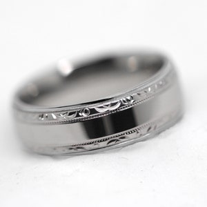 May include: A silver wedding band with a decorative engraved design around the edge.