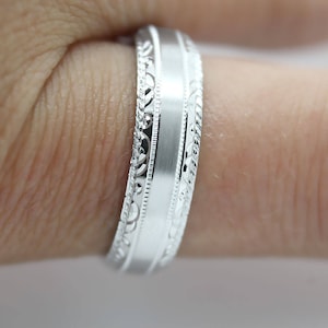 May include: A silver wedding band with a brushed finish and a decorative patterned edge.