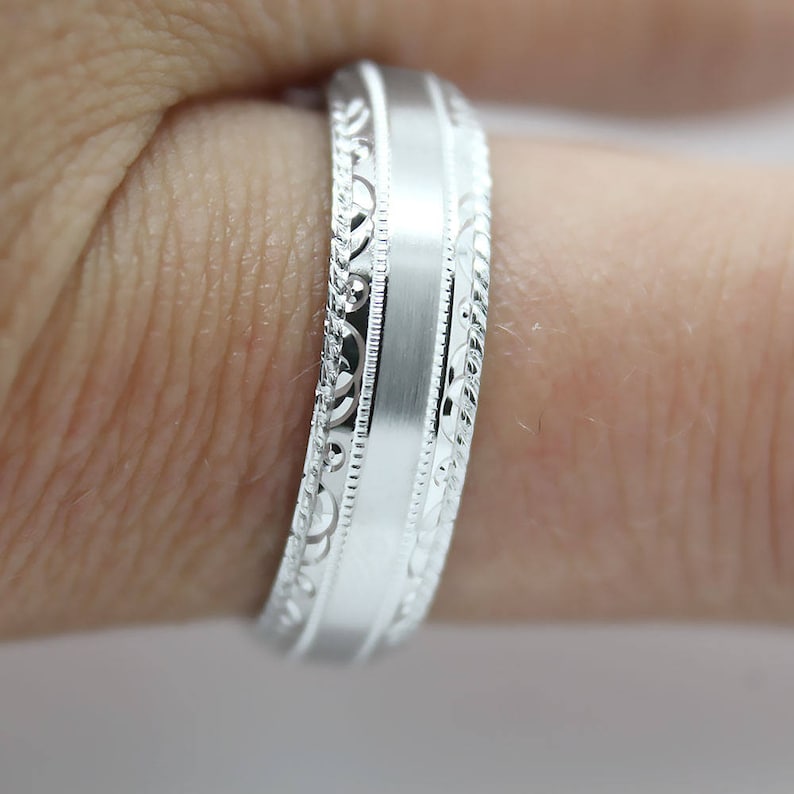 May include: A silver wedding band with a brushed finish and a decorative patterned edge.
