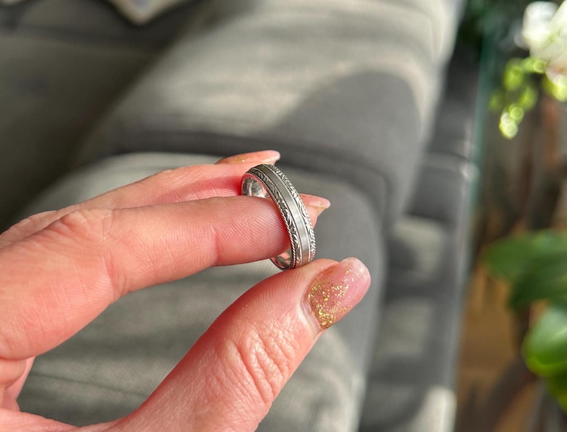 May include: A silver wedding band with a detailed engraved design.