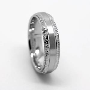 May include: A silver wedding band with a satin finish and a decorative engraved design.