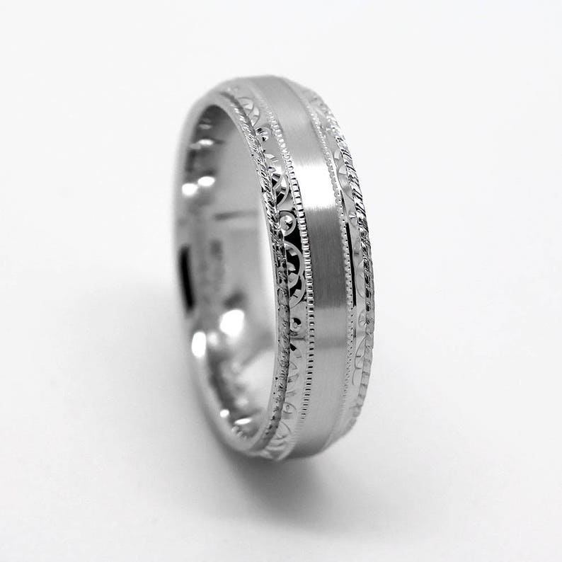 May include: A silver wedding band with a satin finish and a decorative engraved design.