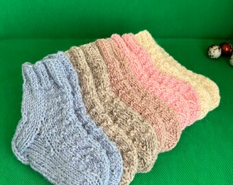 May include: Four pairs of knitted baby socks in different colors: light blue, beige, pink, and cream. The socks are folded and stacked on top of each other.