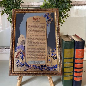 May include: A framed vintage print of a poem titled "Home" by Edgar A. Guest, displayed on a small wooden easel. The artwork features a gold frame, a blue and gold illustration, and the poem's text. Three antique books stand beside it.