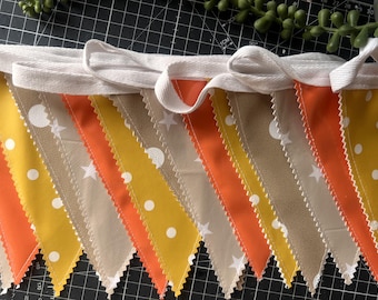 Op de afbeelding: Een stoffen vlaggenlijn met driehoekige wimpels in afwisselende kleuren geel, oranje en beige. De gele wimpels hebben witte stippen, de oranje wimpels zijn effen en de beige wimpels zijn voorzien van witte sterpatronen.