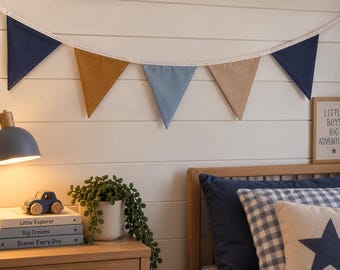 Op de afbeelding: Een stoffen vlaggenlijn met vijf driehoekige vlaggetjes in afwisselende kleuren marineblauw, mosterdgeel, lichtblauw en beige, bevestigd aan een wit koord. De vlaggenlijn hangt horizontaal tegen een witte muur.