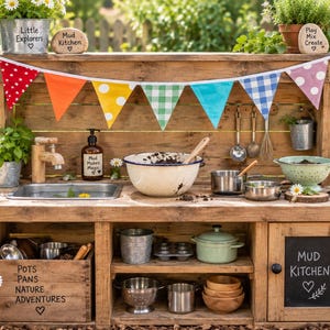 May include: A wooden outdoor mud kitchen featuring a sink, faucet, and shelves stocked with metal pots, pans, bowls, and utensils. The unit is decorated with a colorful fabric bunting and includes chalkboard labels reading Mud Kitchen and Pots Pans.