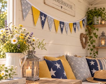 May include: A decorative bunting banner featuring alternating triangular flags in navy blue with white stars, solid mustard yellow, and grey with a white geometric star pattern, suspended against a white wooden wall with a Summerhouse sign.