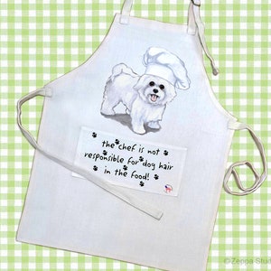 May include: White cotton apron with a white dog wearing a chef's hat. The apron has a pocket with the text "the chef is not responsible for dog hair in the food!"
