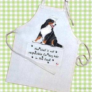 May include: White kitchen apron with a black and white Bernese Mountain Dog wearing a chef's hat. The text on the apron reads "the chef is not responsible for dog hair in the food!"