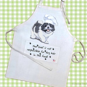 May include: White cotton apron with a black and white dog wearing a chef's hat. The apron has a pocket with the text "the chef is not responsible for dog hair in the food!"