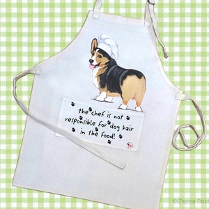 May include: White kitchen apron with a cartoon image of a corgi wearing a chef's hat. The text on the apron reads "the chef is not responsible for dog hair in the food!"